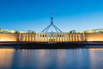 A photo of Parliament House in Canberra at twilight with the building and lights reflected in the lake at the front.