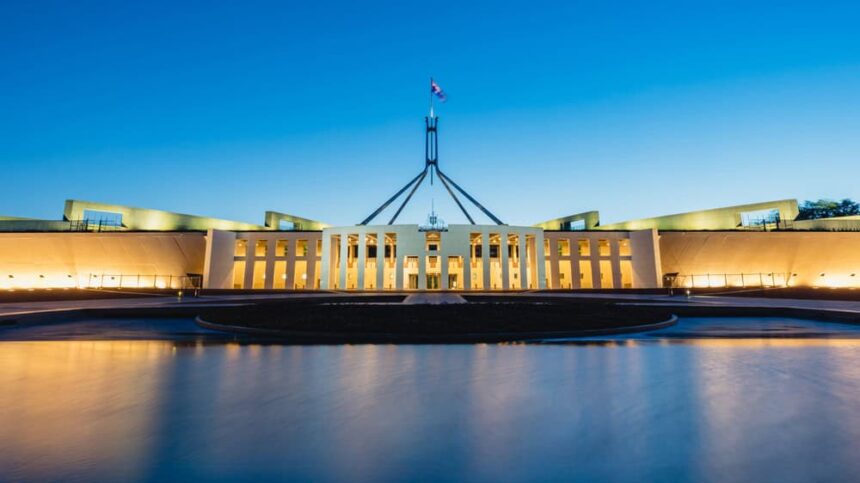 A photo of Parliament House in Canberra at twilight with the building and lights reflected in the lake at the front.