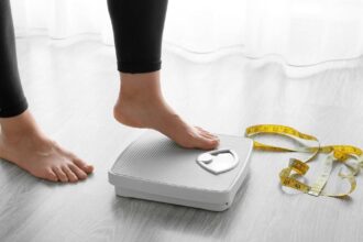 Image of person standing on a scale next to a roll of measuring tape