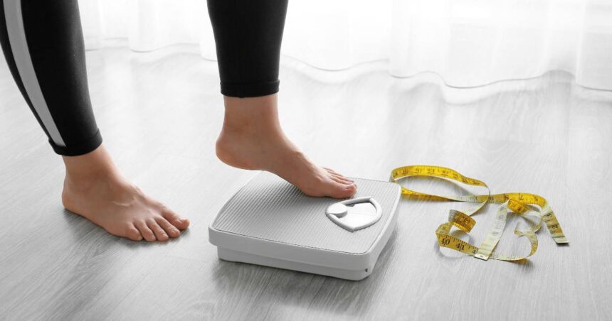 Image of person standing on a scale next to a roll of measuring tape