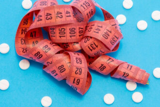 A tape measure laying on a blue background with scattered white pills