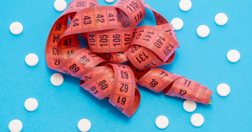 A tape measure laying on a blue background with scattered white pills