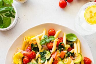 A serving of pasta primavera on a plate topped with fresh herbs.