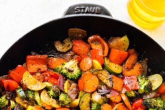 A cast iron skillet of sautéed vegetables including broccoli, carrots, onion, tomatoes, zucchini, and more.