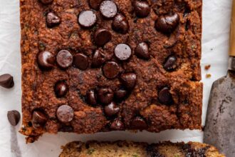 Three slices of vegan zucchini bread with chocolate chips leaning against one another near a loaf.