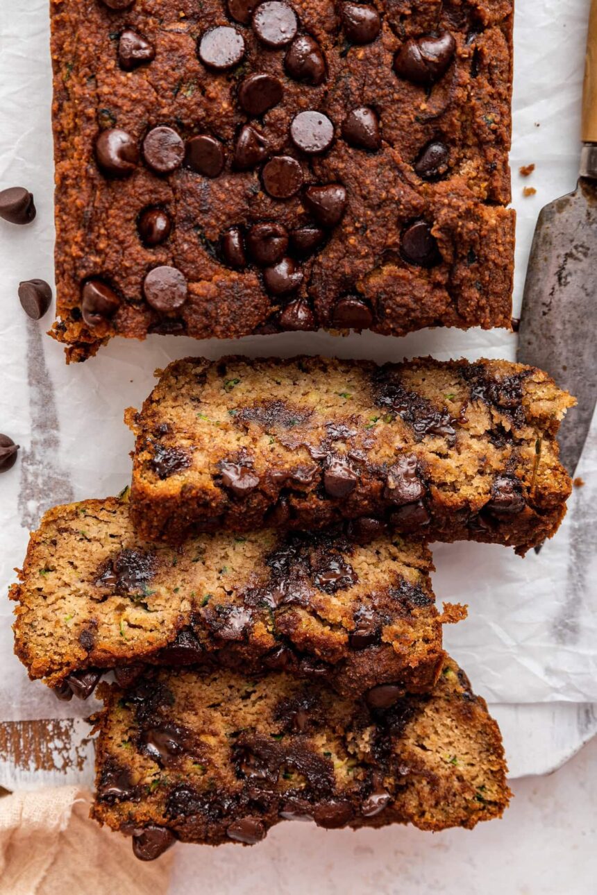 Three slices of vegan zucchini bread with chocolate chips leaning against one another near a loaf.