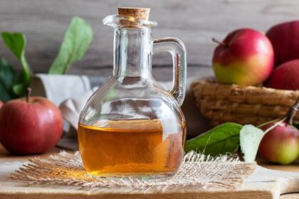 Glass bottle of apple cider vinegar in front of basket with apples