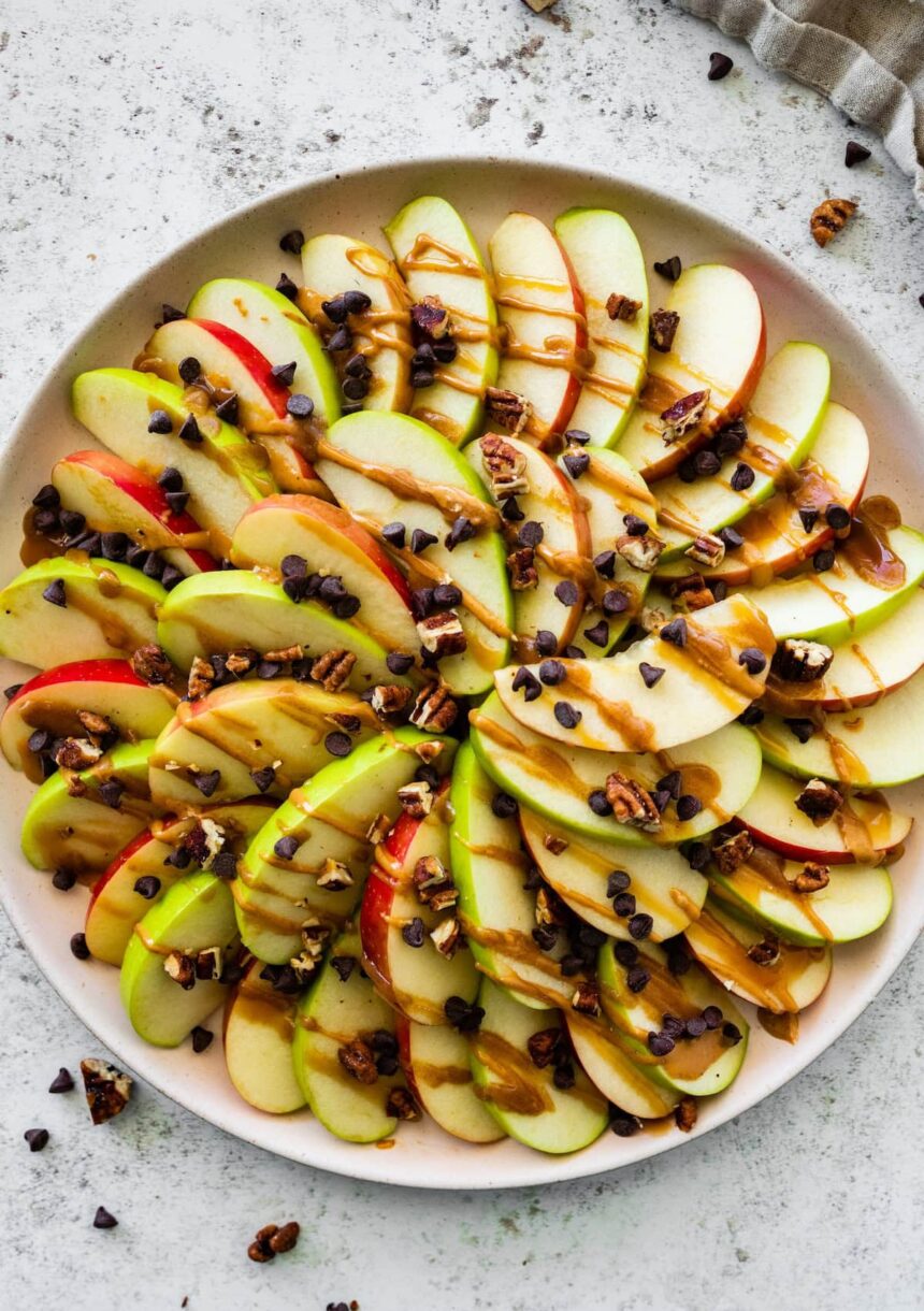 A large plate of apple nachos topped with a date caramel drizzle, mini chocolate chips, and pecans.