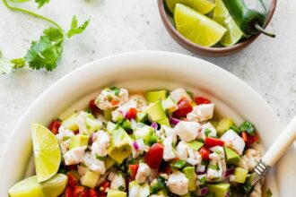 A large white bowl of ceviche with fresh fish, avocado, tomato, cucumber, and avocado.