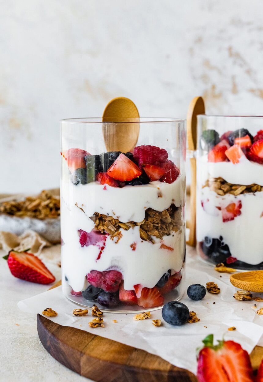 Two glass cups of fruit and yogurt parfaits. The cups are layered with fruit, yogurt, granola, then yogurt again and more fruit on top.