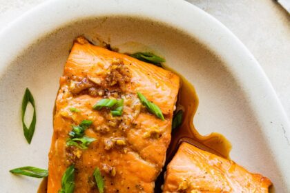 Two maple glazed salmon filets on a plate topped with green onion.