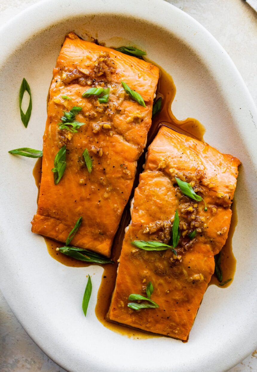 Two maple glazed salmon filets on a plate topped with green onion.