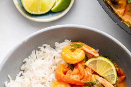 A serving of coconut shrimp curry with white rice in a small bowl.