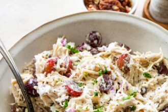 A sonoma chicken salad in a large bowl with ingredients like grapes, shredded chicken, pecans, and more.