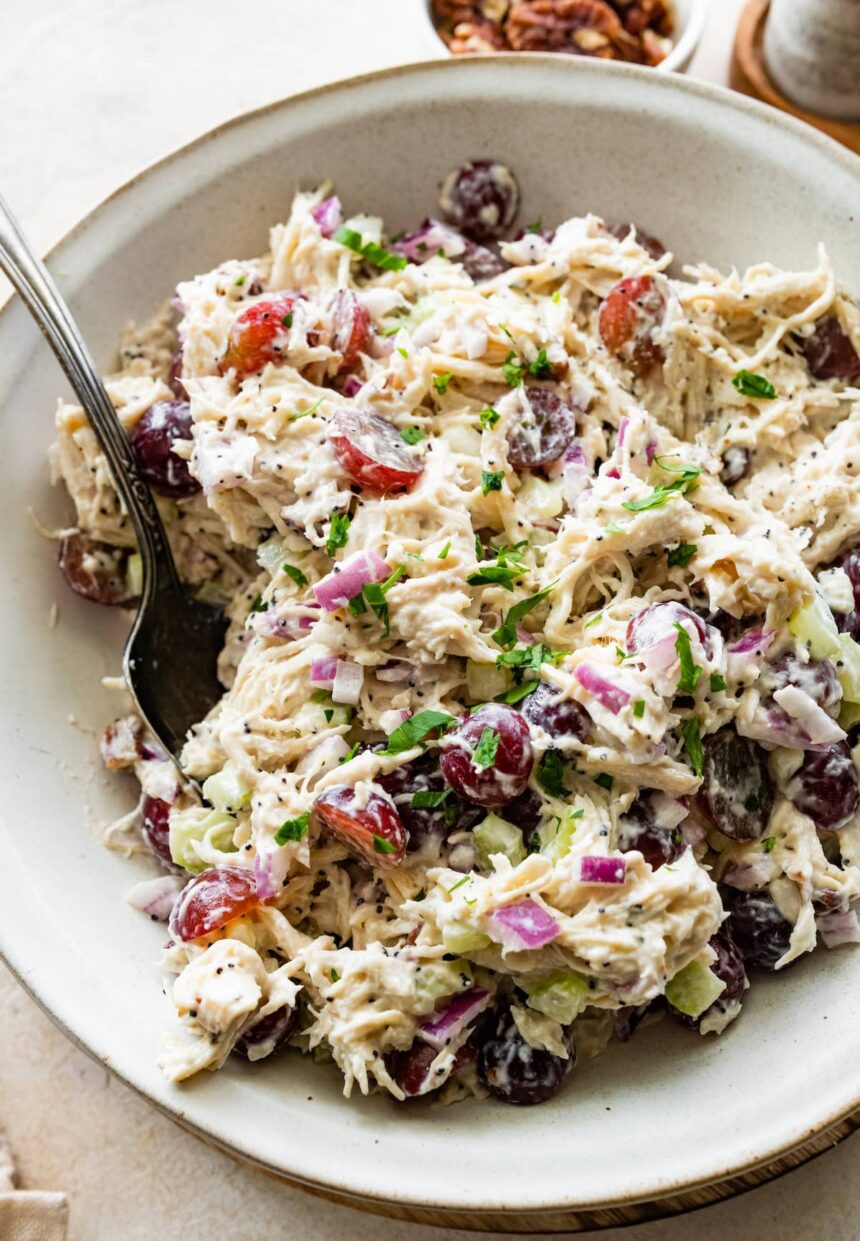 A sonoma chicken salad in a large bowl with ingredients like grapes, shredded chicken, pecans, and more.