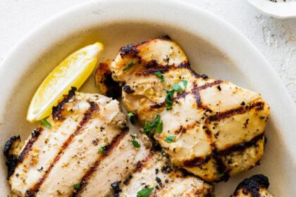 Multiple yogurt marinated chicken thighs on a plate with lemon wedges on the side.