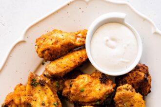 A large plate of air fried chicken wings topped with fresh herbs with a side of ranch.