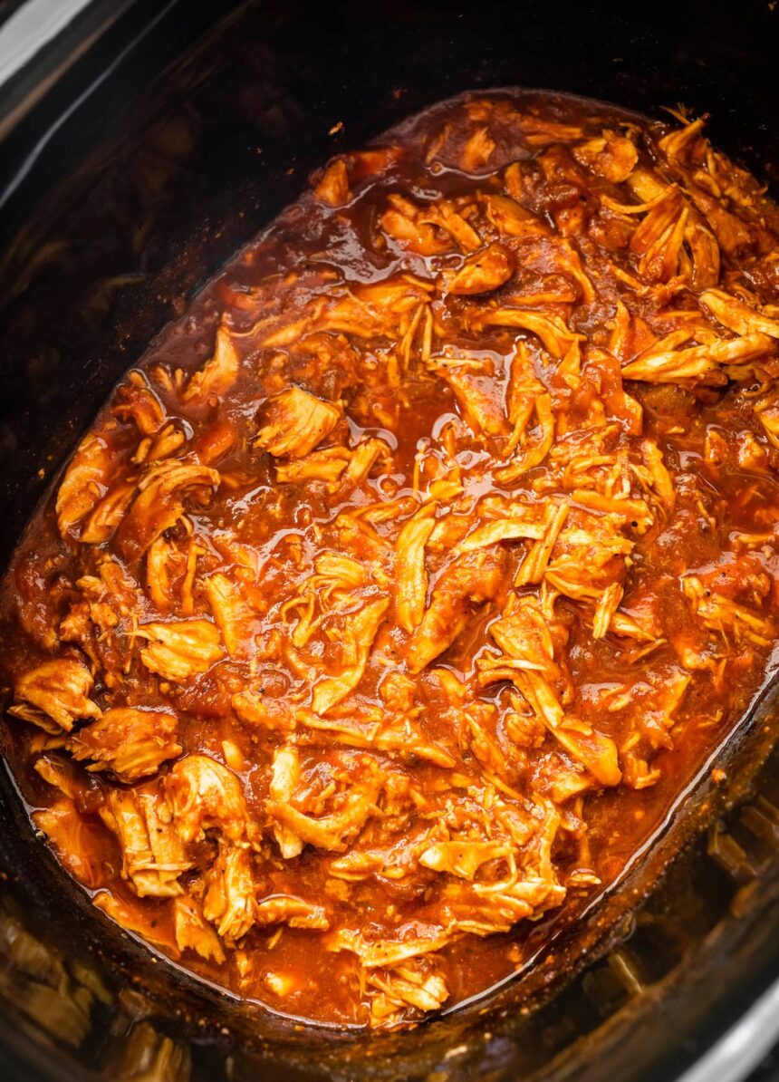 A slow cooker pot full of bbq shredded chicken.