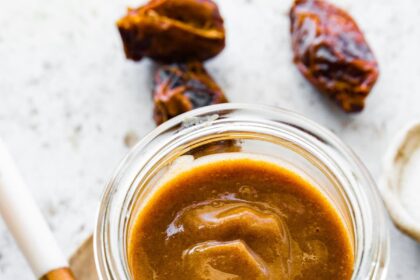 A glass jar of date caramel near a wooden spoon.