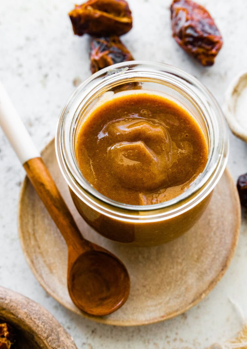 A glass jar of date caramel near a wooden spoon.