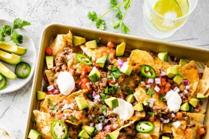 Loaded nachos on a baking tray with meat, jalapeños, sour cream, avocado, cheese, and more.