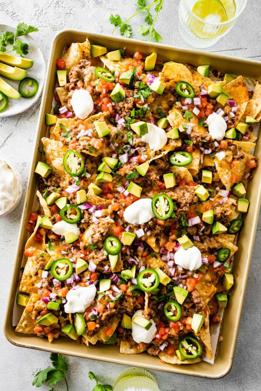 Loaded nachos on a baking tray with meat, jalapeños, sour cream, avocado, cheese, and more.