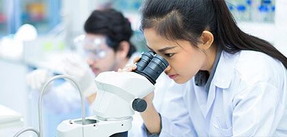 A young female researcher is looking into a double-lens microscope.