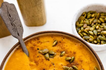 A bowl of autumn soup topped with cracked black pepper, and pepitas.