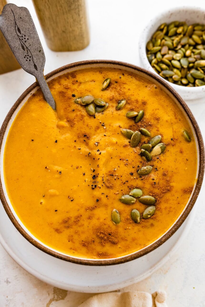 A bowl of autumn soup topped with cracked black pepper, and pepitas.