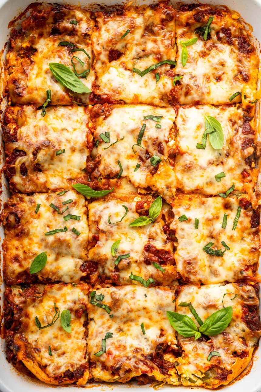 Healthy lasagna in a baking dish, cut into squares, and garnished with fresh basil and parsley.