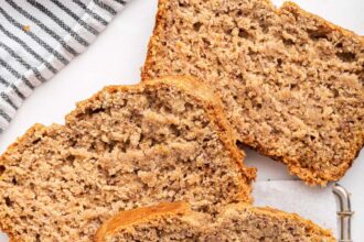 Oat flour banana bread on a cooling wire rack with three slices near the loaf.