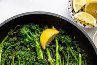 A pan of sautéed broccolini with lemon wedges and red pepper flakes.