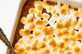 Sweet potato casserole in a square baking dish with a portion missing in the corner where a metal spoon is.