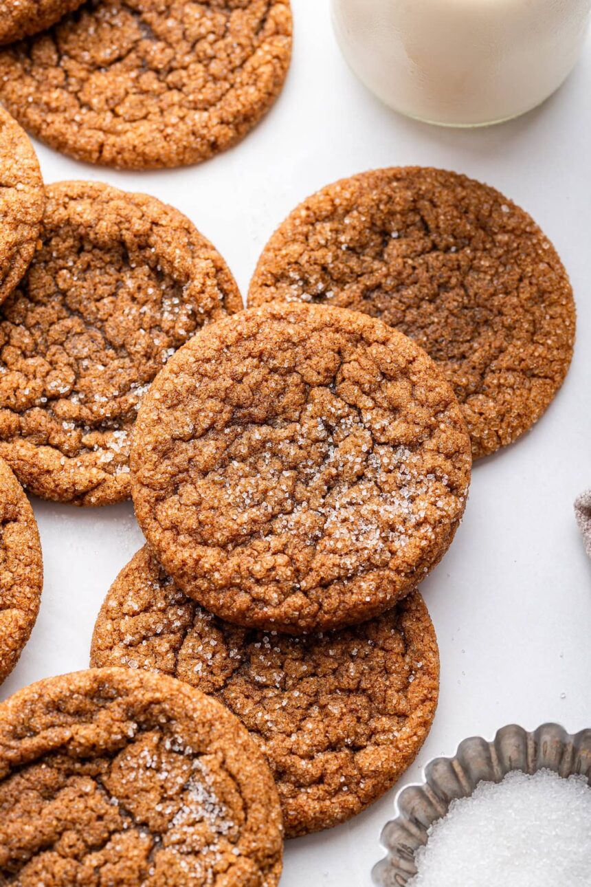 Multiple molasses cookies sprinkled with cane sugar with a glass of milk in the background.