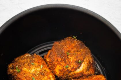 Four bone-in chicken thighs cooked in the basket of an air fryer topped with fresh parsley.