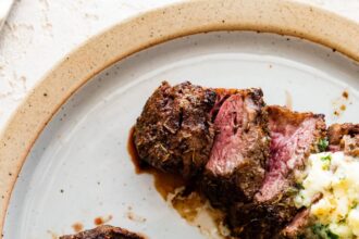 Two filet mignon pieces sliced on a white plate topped with garlic butter.