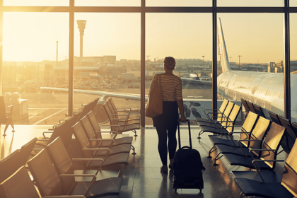 Shot of a woman at the airport looking out of the window while pulling her case