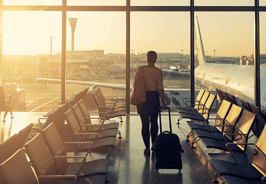 Shot of a woman at the airport looking out of the window while pulling her case