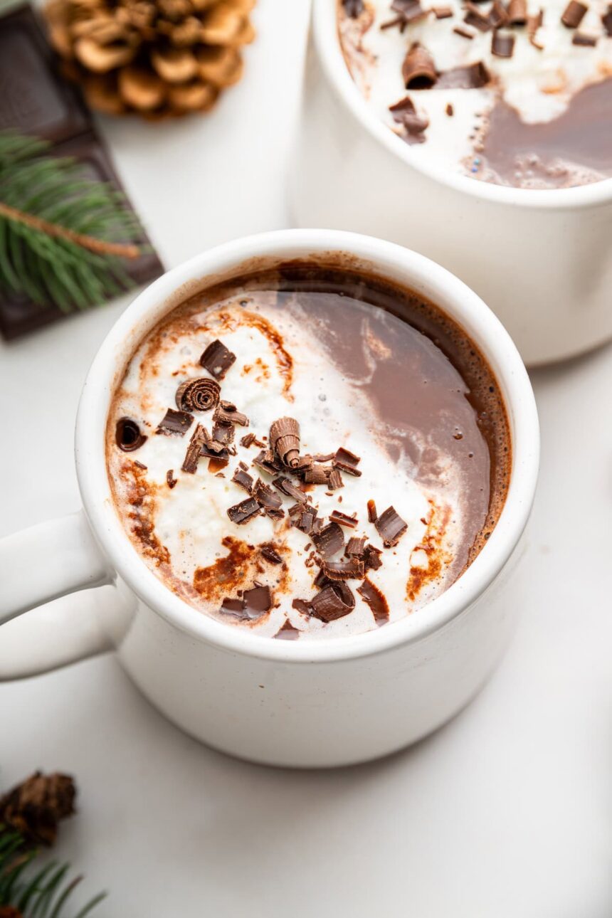 Two white mugs of hot chocolate topped with a little whip cream and chocolate shavings.