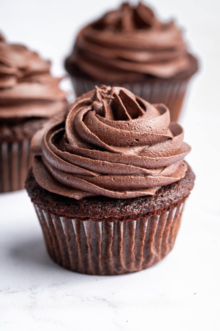 Three chocolate cupcakes topped with chocolate buttercream frosting.