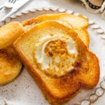 A slice of toast on a plate with the center cut out of it. A cooked egg is in the center of the slice of bread.