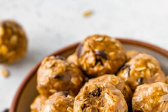 No bake energy balls piled in a bowl, with one ball showing a bite taken out of it.