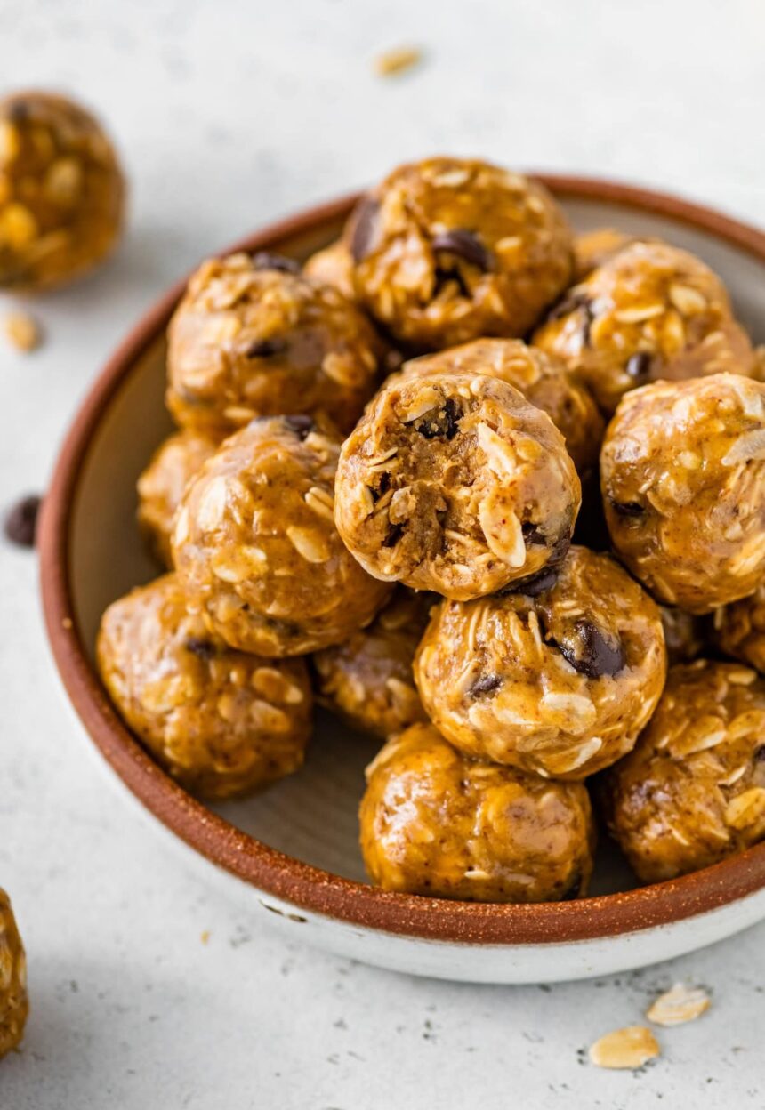 No bake energy balls piled in a bowl, with one ball showing a bite taken out of it.