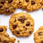 Multiple peanut butter oatmeal cookies with chocolate chips spread out on a table. One of the cookies has a bite taken out of it.