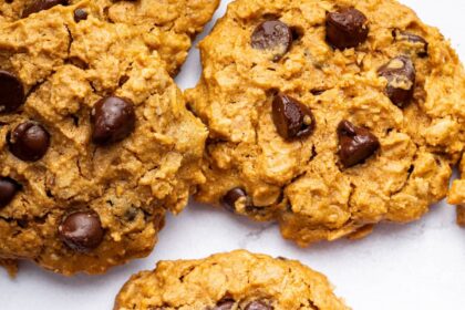 Multiple peanut butter oatmeal cookies with chocolate chips spread out on a table. One of the cookies has a bite taken out of it.