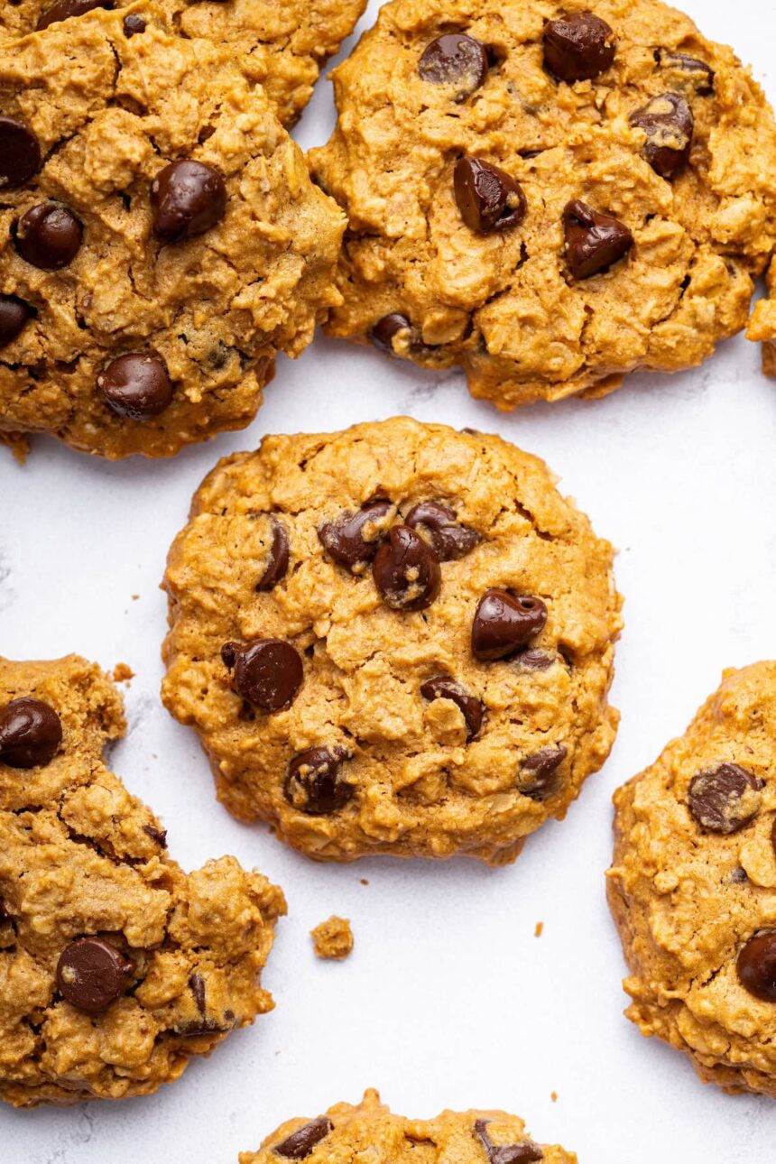 Multiple peanut butter oatmeal cookies with chocolate chips spread out on a table. One of the cookies has a bite taken out of it.