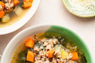 Sausage and kale soup served up in a green and white soup bowl.