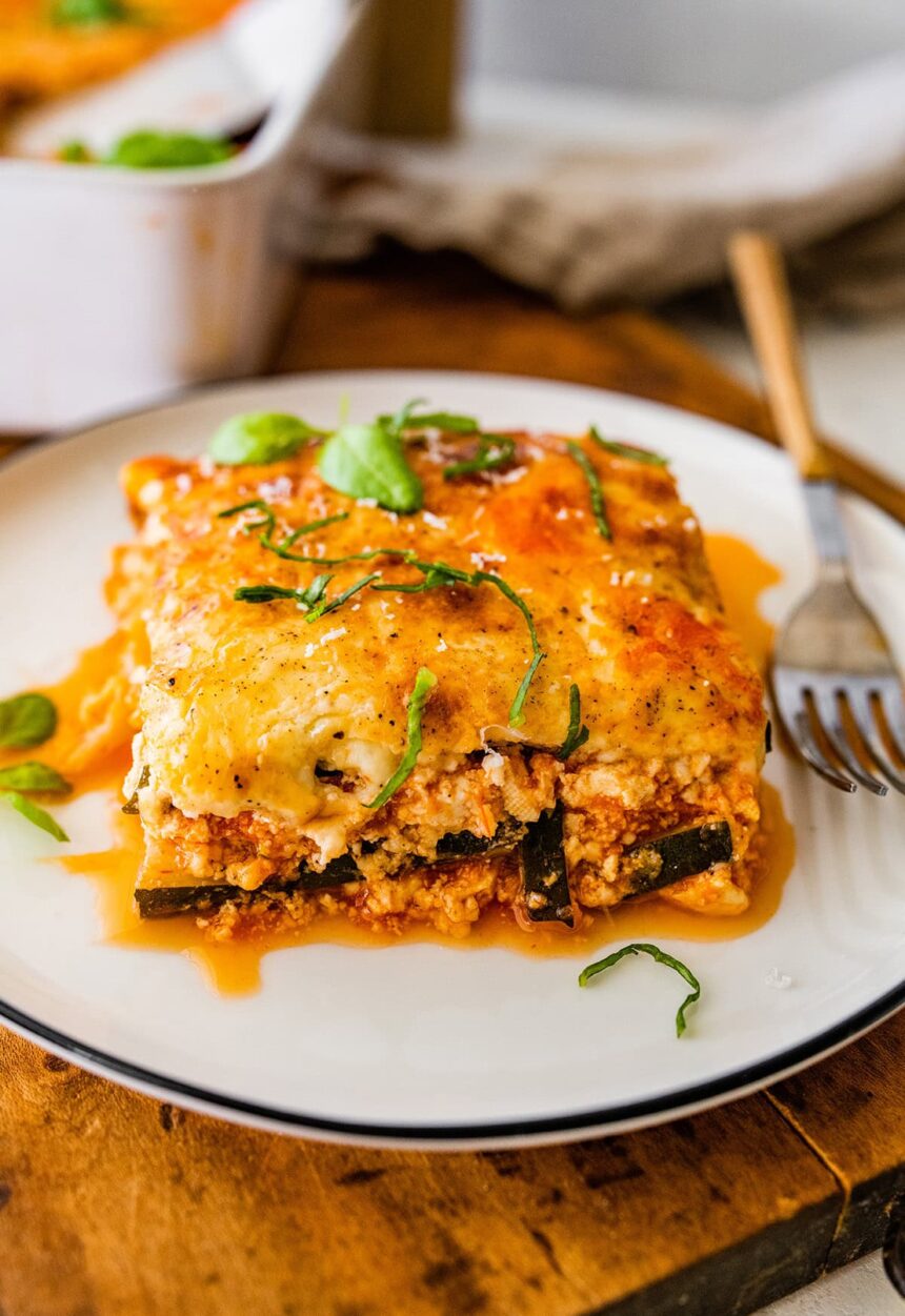 A serving of vegetarian tofu lasagna made with zucchini noodles on a white plate with a fork.