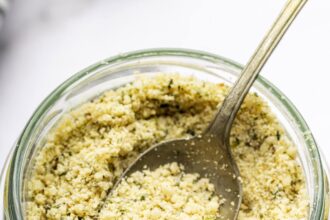 A vegan parmesan cheese made with hemp seeds in a glass mason jar with a metal spoon.