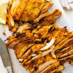 Chicken Shawarma sliced on a cutting board. There is a knife and lemon slices next to the chicken.